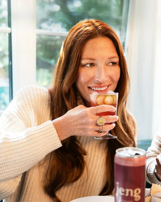 A woman smiling while sipping Jeng's alcohol-free Rhubarb Cucumber Spritz cocktail, enjoying a refreshing moment.