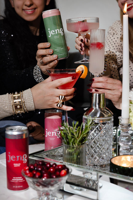 Group of friends toasting Jeng THC cocktails at a candlelit bachelorette party table with cocktail shaker and fresh herbs.