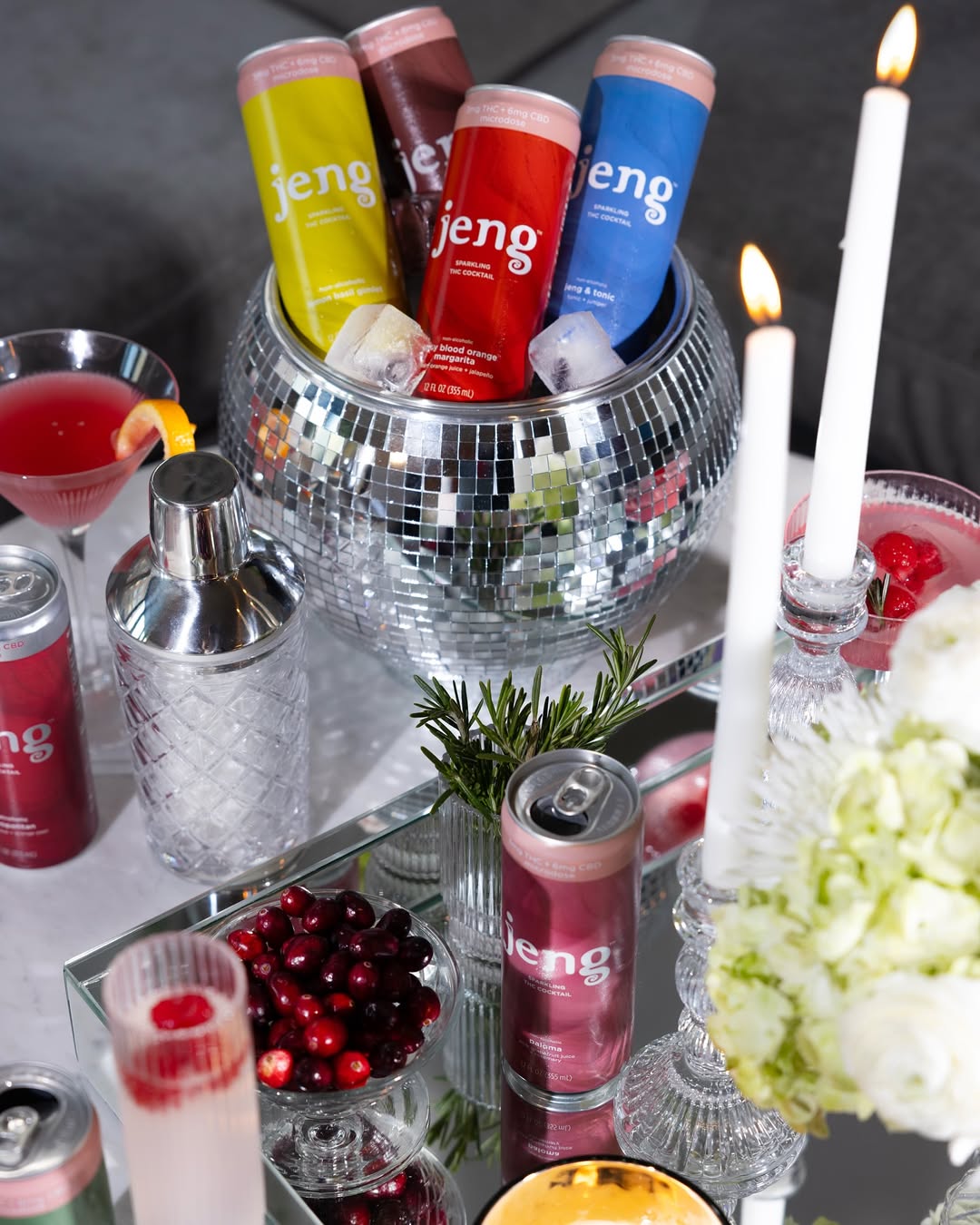 Jeng THC-free sparkling cocktails chilling in a disco ball cooler with candles, cranberries, and festive glassware on display.