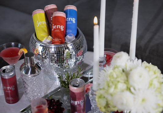 Jeng THC cocktail cans chilling in a disco ball ice bucket beside candles and cocktail glasses.
