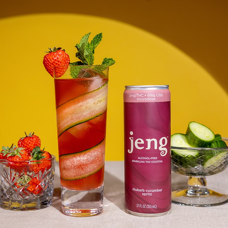 Hand garnishing a blood orange cocktail beside a Jeng Spicy Blood Orange Margarita can.