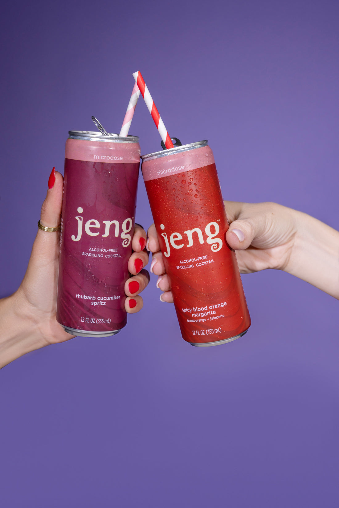 Two hands clinking a Jeng Rhubarb Cucumber Spritz can and a Spicy Blood Orange Margarita can, each with a straw, during Dry January.