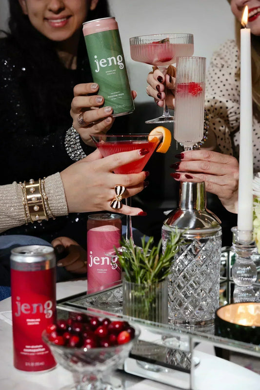 Friends clinking festive cocktails and cans of Jeng sparkling cocktails at an elegant Galentine’s gathering.