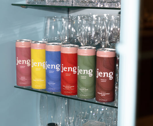 Jeng sparkling cocktails in colorful cans on a bar shelf with crystal glasses and bar tools.