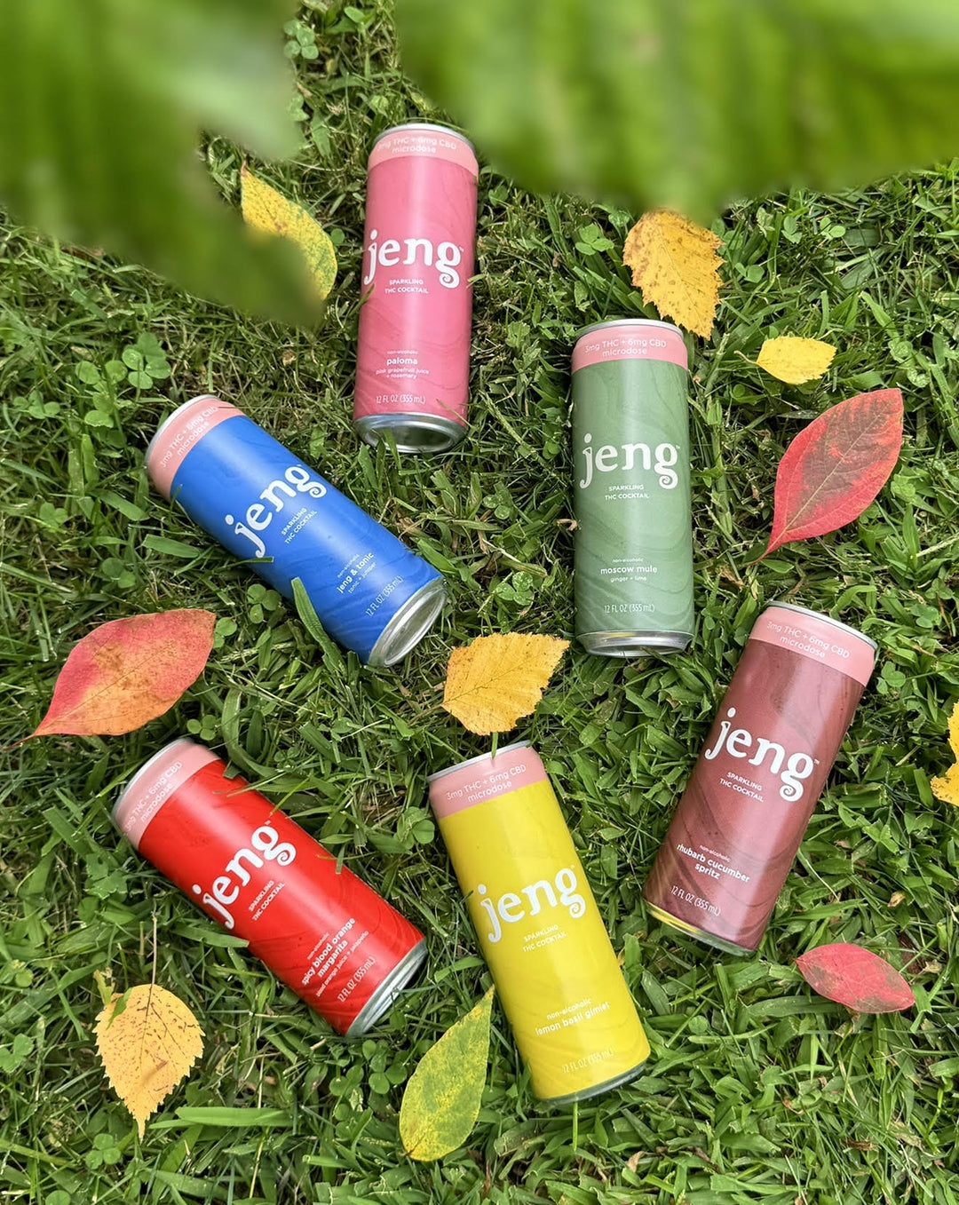 Colorful Jeng THC cocktail cans scattered on green grass with autumn leaves.