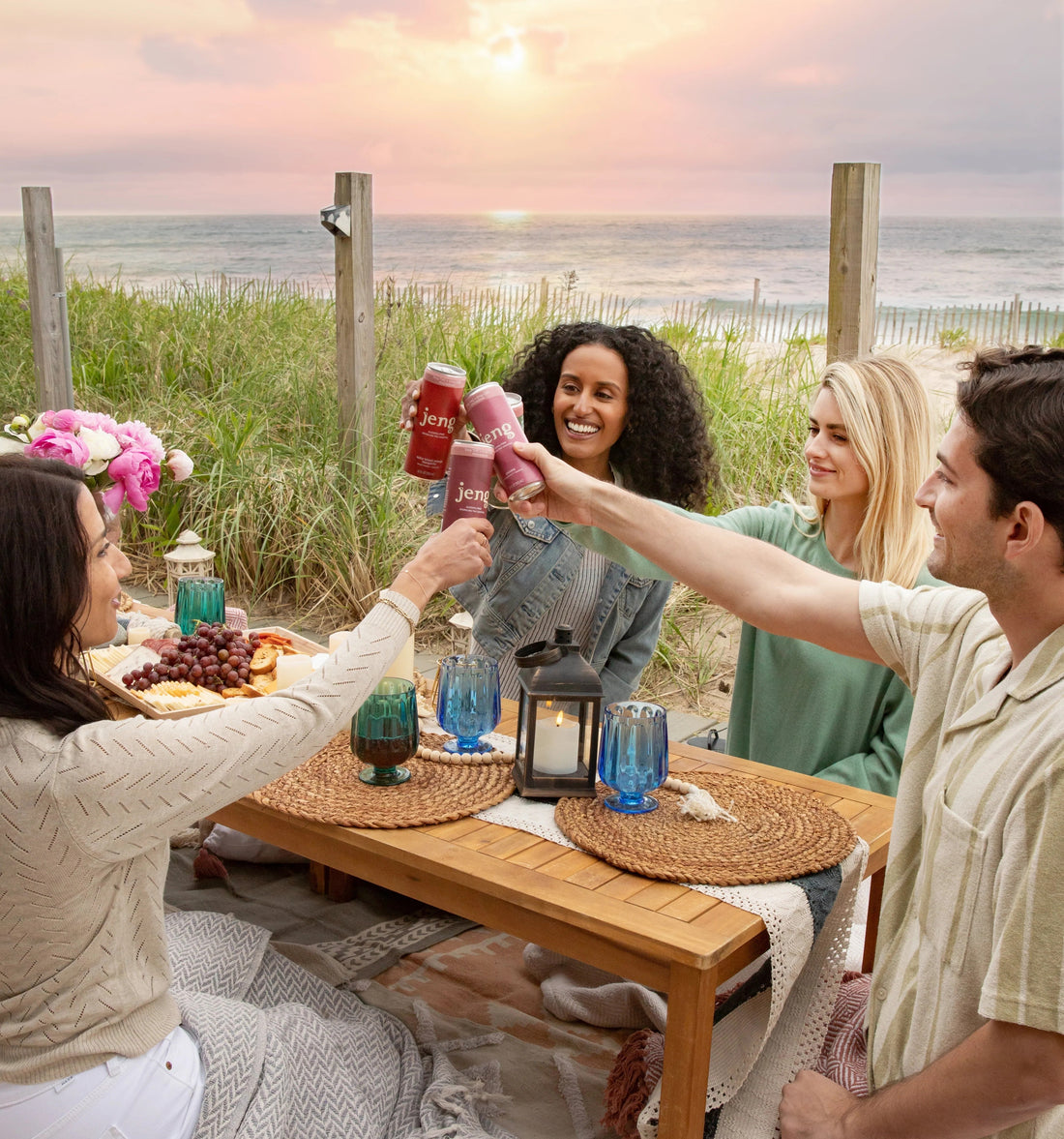  Friends toasting with Jeng sparkling THC cocktails at a cozy beach picnic during sunset.