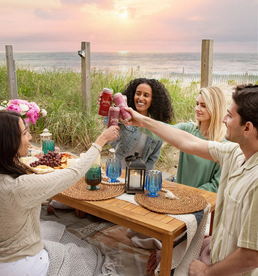  Friends toasting with Jeng sparkling THC cocktails at a cozy beach picnic during sunset.