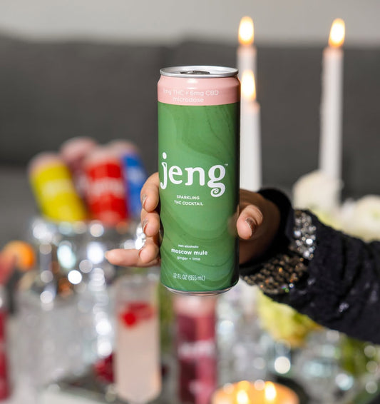 Hand holding a green Jeng Moscow Mule THC cocktail can at a festive, candlelit St. Patrick’s Day table.