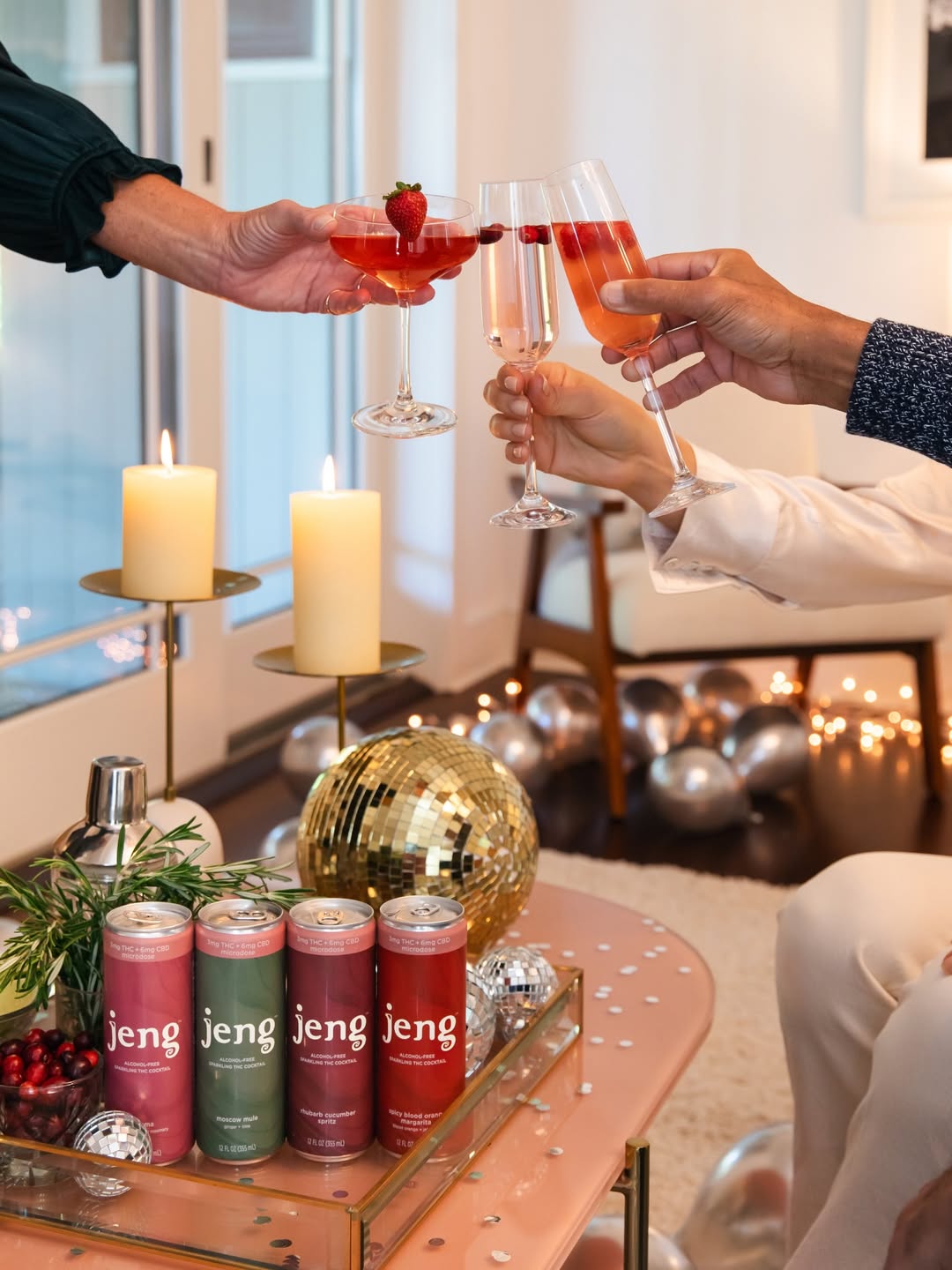 Jeng cans and festive cocktails arranged on a holiday table as guests toast with sparkling glasses in a warm, celebratory setting.