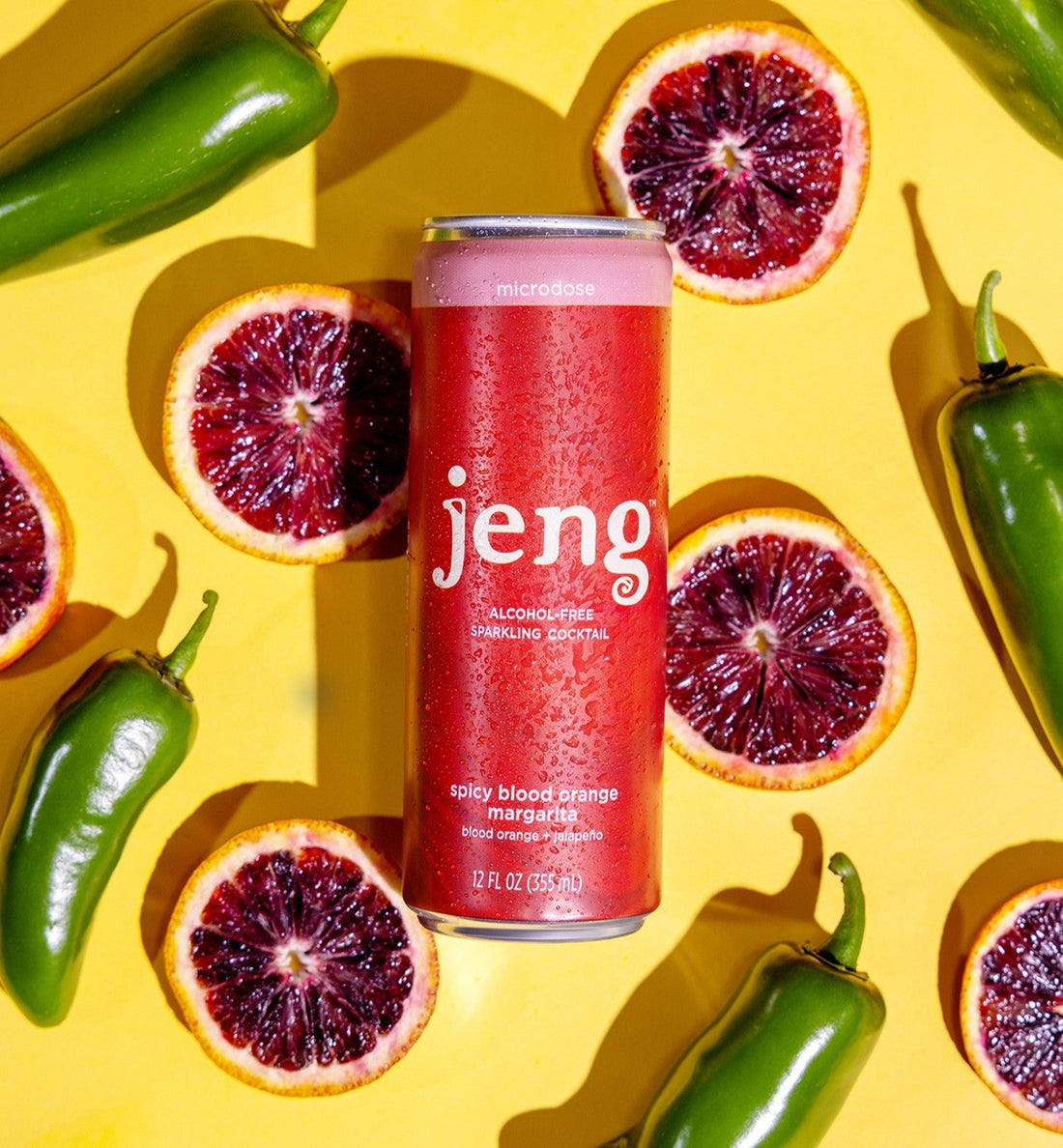 Jeng sparkling cocktail can surrounded by blood orange slices and jalapeño peppers on yellow.