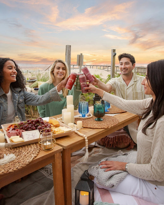 Friends toasting with sparkling non-alcoholic drinks at a beachside dinner during a warm spring sunset