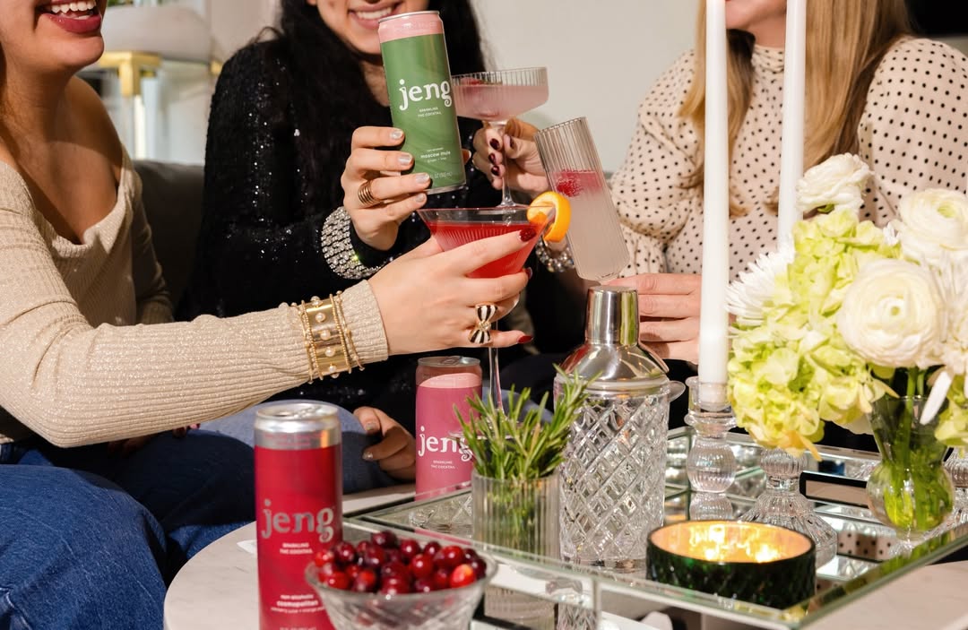 : Friends enjoying festive holiday cocktails with Jeng zero-proof THC cans and citrus garnishes on a decorated party table.