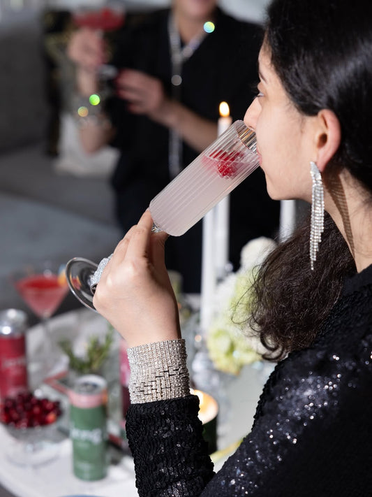 Woman sipping a sparkling pink cocktail at a festive table with Jeng cans visible in the background.