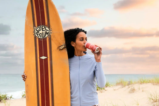 A woman surfer enjoying a can of Jeng THC-infused sparkling beverage while preparing for her adventure.